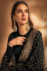 Woman wearing a black outfit with gold embroidery and jewelry against a warm-toned background