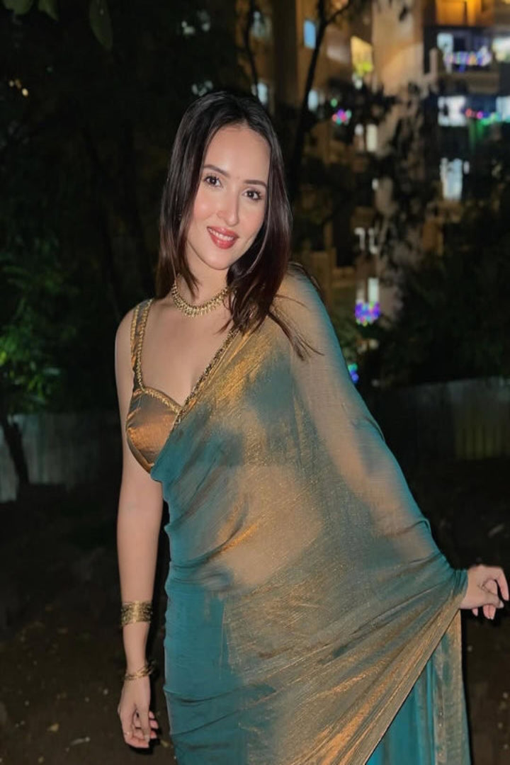 Woman in a green saree with gold blouse standing outdoors at night.