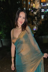 Woman in a green saree with gold blouse standing outdoors at night.