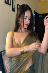 Woman in a gold and green saree adjusting her saree in a room.
