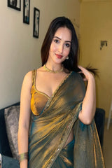 Woman in a traditional saree with gold and green colors indoors.
