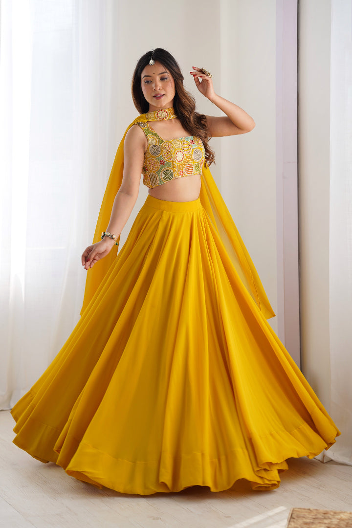 Woman wearing a yellow traditional outfit with a floral top and flowing skirt in a bright room.