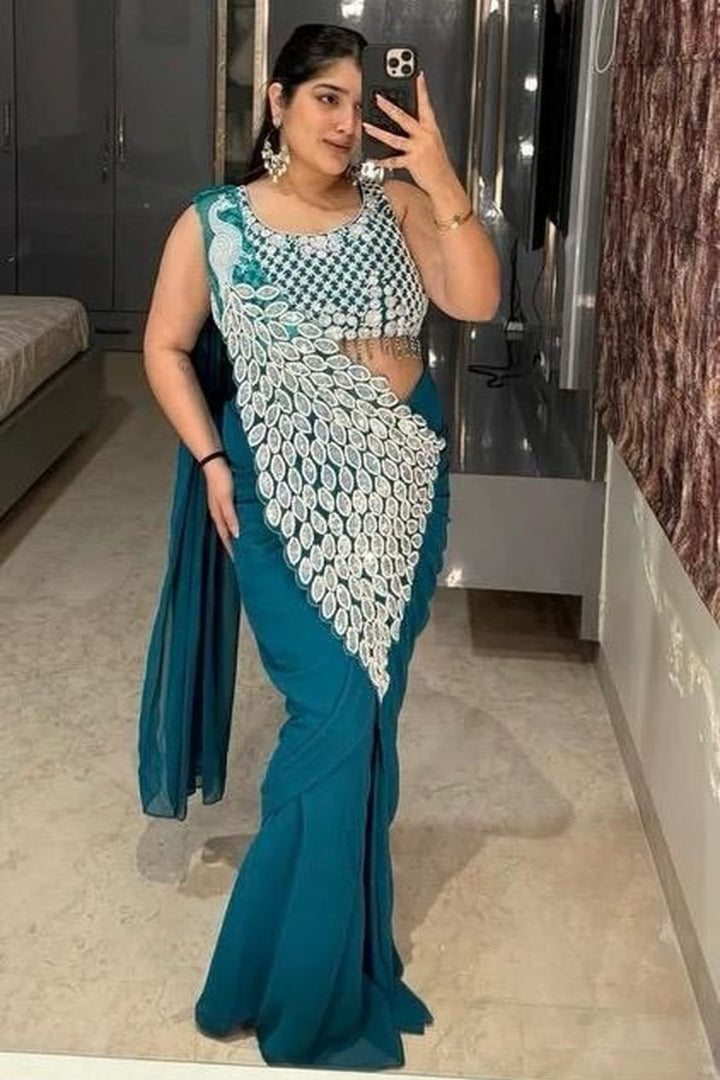 Woman in a teal saree with a white blouse taking a mirror selfie.