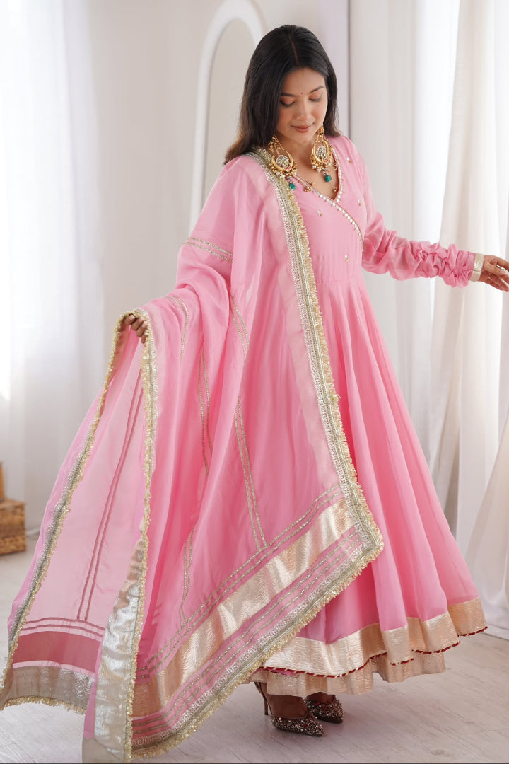 Woman wearing a pink traditional outfit with gold accents in a bright room.
