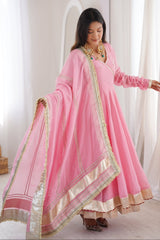Woman wearing a pink traditional outfit with gold accents in a bright room.