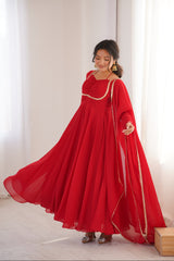 Woman wearing a long red dress with gold trim in a room with white curtains.