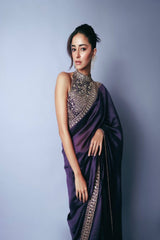 Woman wearing a purple saree with intricate silver embroidery against a gray background