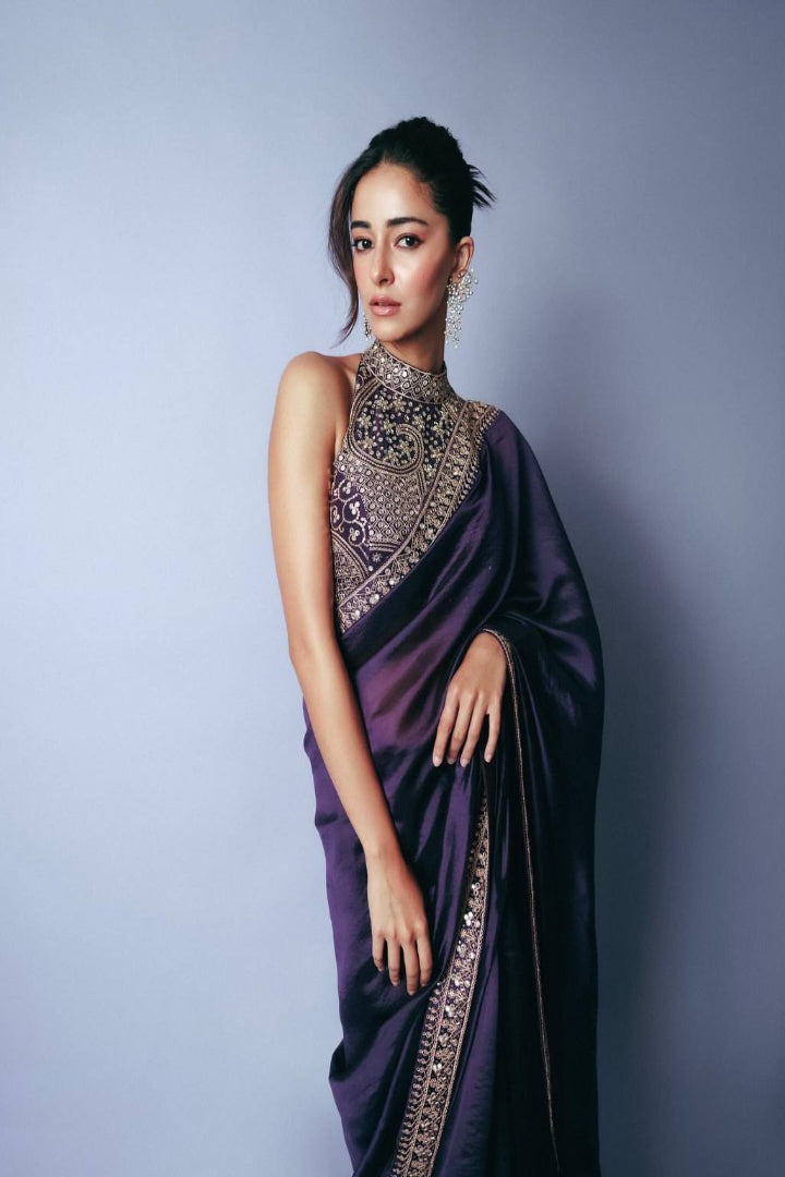 Woman wearing a purple saree with intricate silver embroidery against a gray background