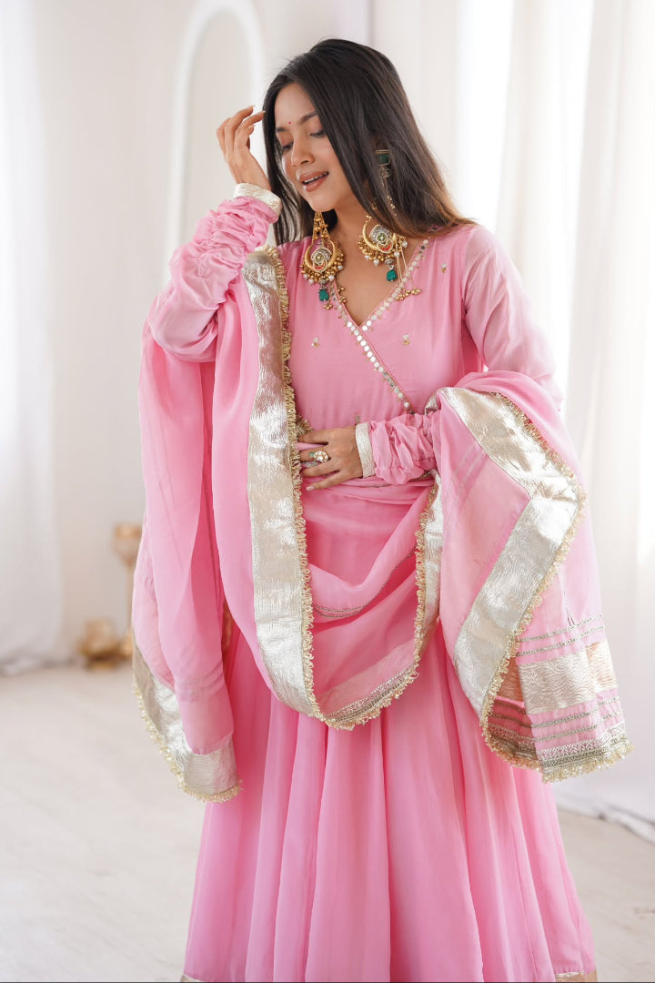 Woman wearing a pink traditional outfit with gold accents in a bright room.