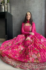 Woman in a bright pink traditional outfit with floral patterns sitting on the floor against a gray wall.