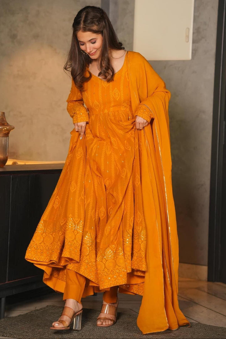 Woman wearing a mustard yellow traditional outfit with a long drape in an indoor setting.