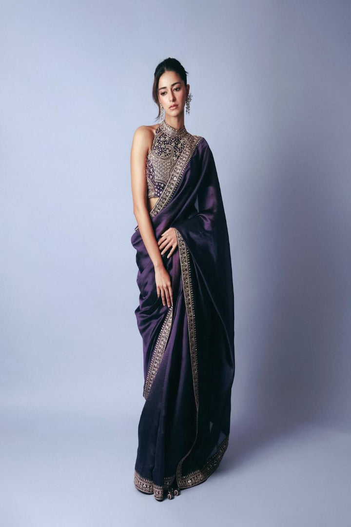 Woman wearing a purple saree with intricate designs on a light gray background