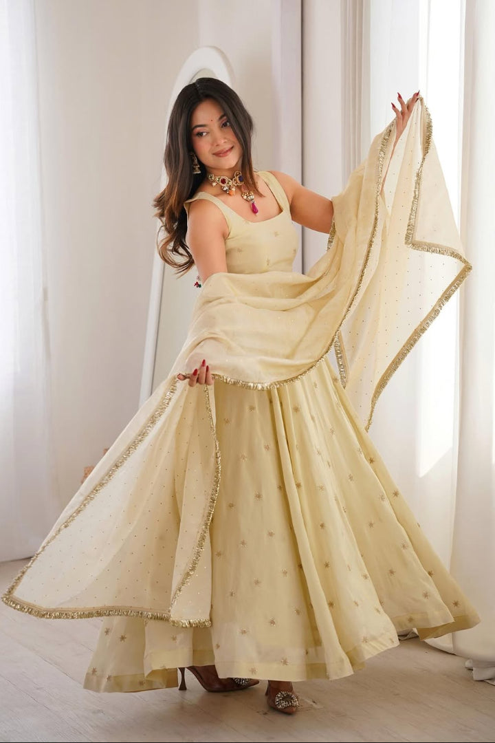 Woman in a beige traditional outfit with a matching dupatta against a white curtain background