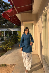 Woman in a blue outfit standing outside a building with a red awning.