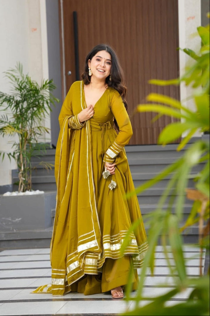 Woman in a yellow traditional outfit standing outdoors with plants and a door in the background