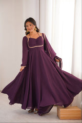 Woman wearing a long purple dress with a matching shawl in a minimalistic setting.