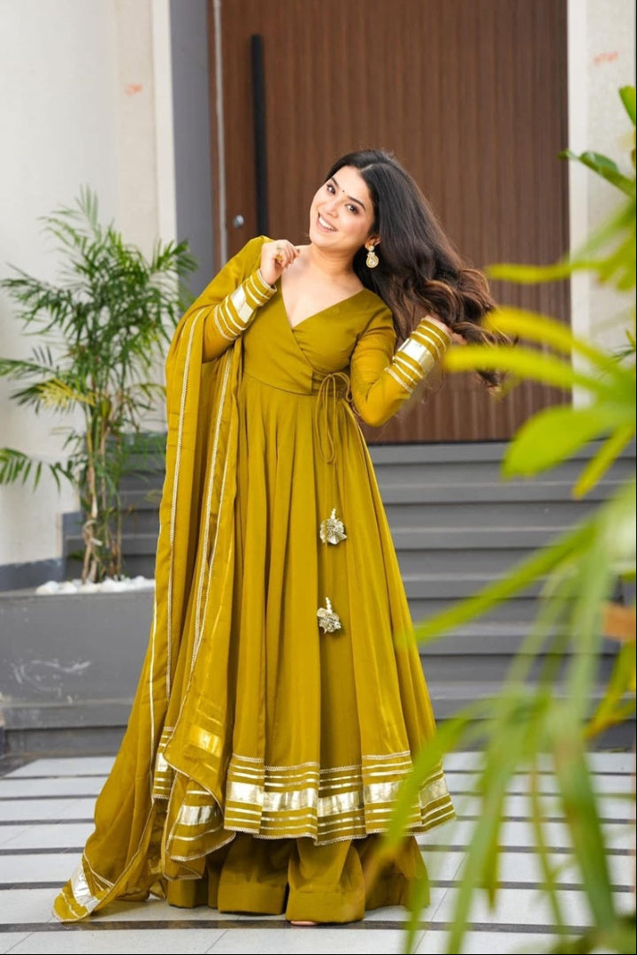 Woman in a yellow traditional outfit standing outdoors with plants and a door in the background
