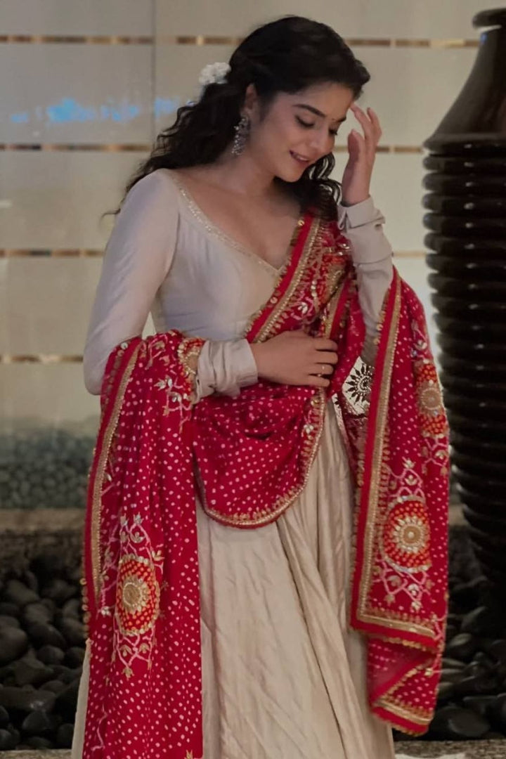 Woman in a traditional outfit with a red and gold shawl against a neutral background