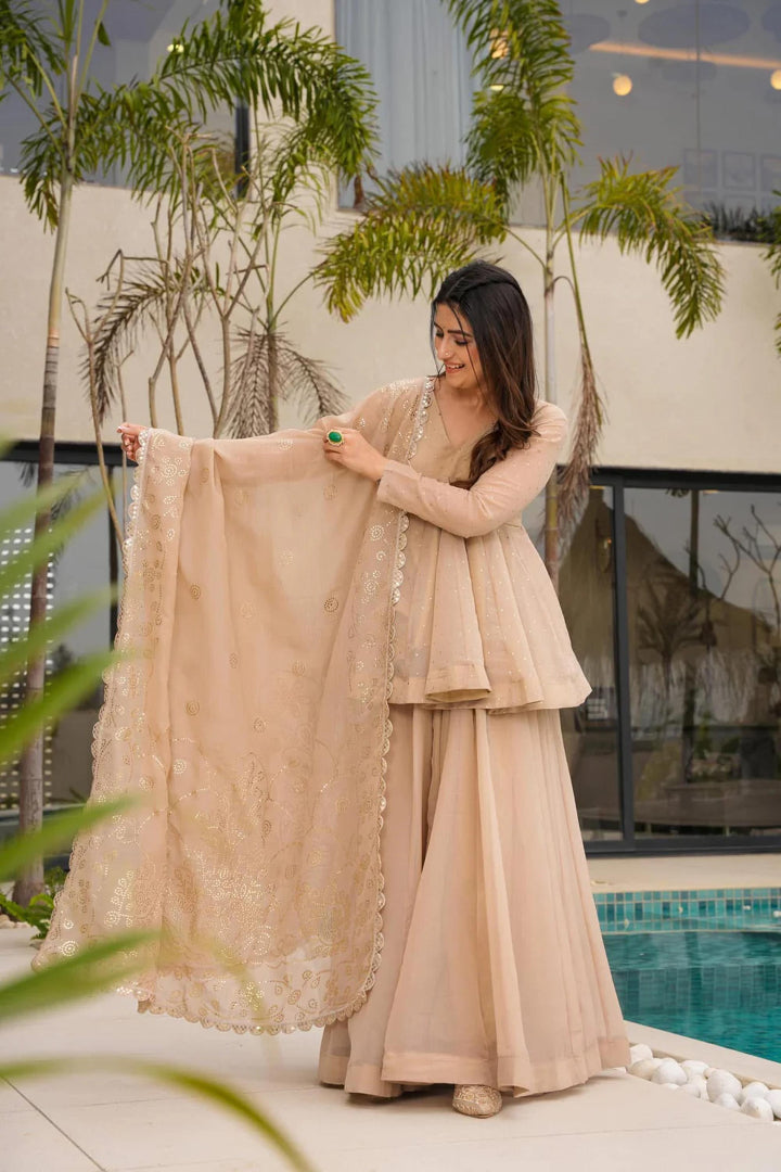 Woman in a beige traditional outfit holding a matching dupatta by a poolside.