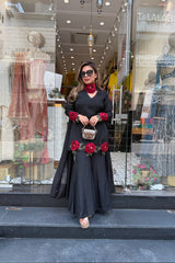 Woman in a black dress with red floral accessories standing in front of a store window.