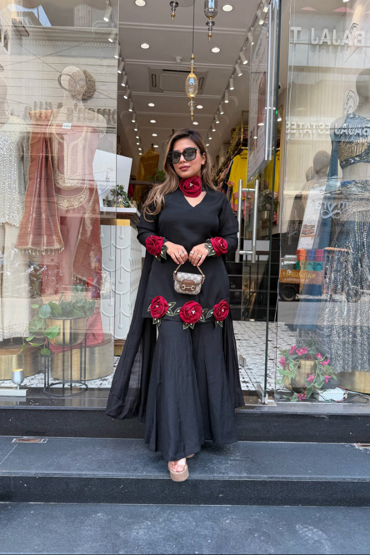 Woman in a black dress with red floral accessories standing in front of a store window.