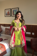 Woman in a green and pink traditional outfit standing in a room with a bed and wall art.
