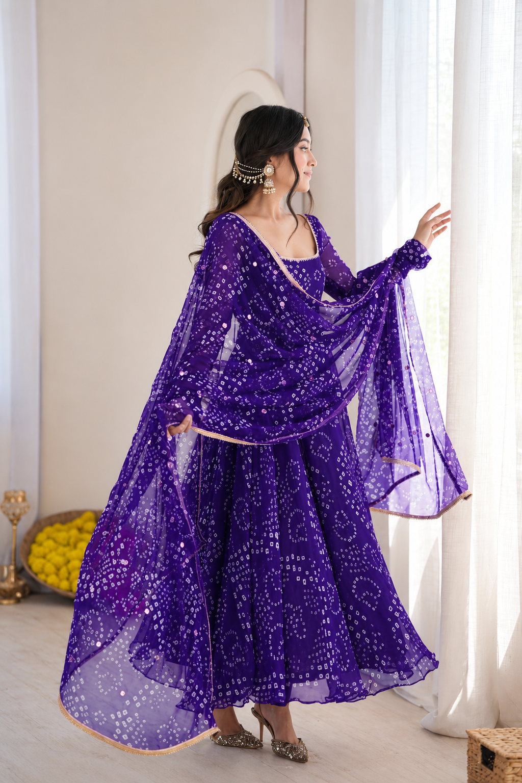 A woman wearing a purple traditional outfit with a matching sheer dupatta and skirt, decorated with white printed motifs, standing in a bright indoor setting with white curtains.