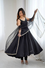 Woman in a black traditional outfit with a sheer dupatta against a white background