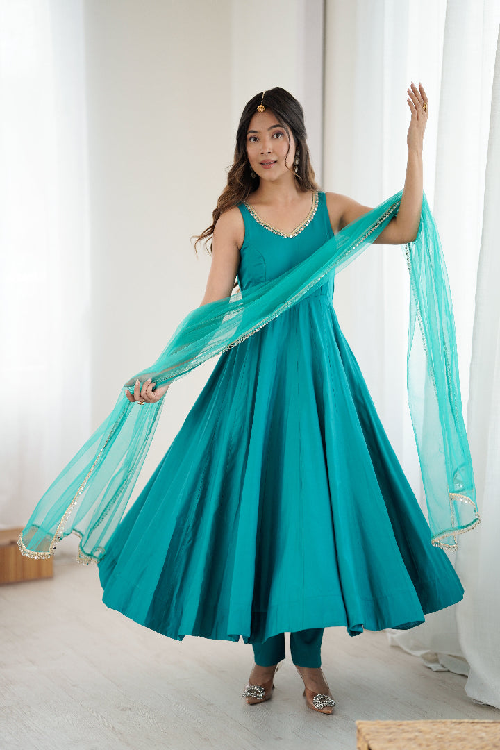 Woman in a teal dress with a matching dupatta standing in a bright room.