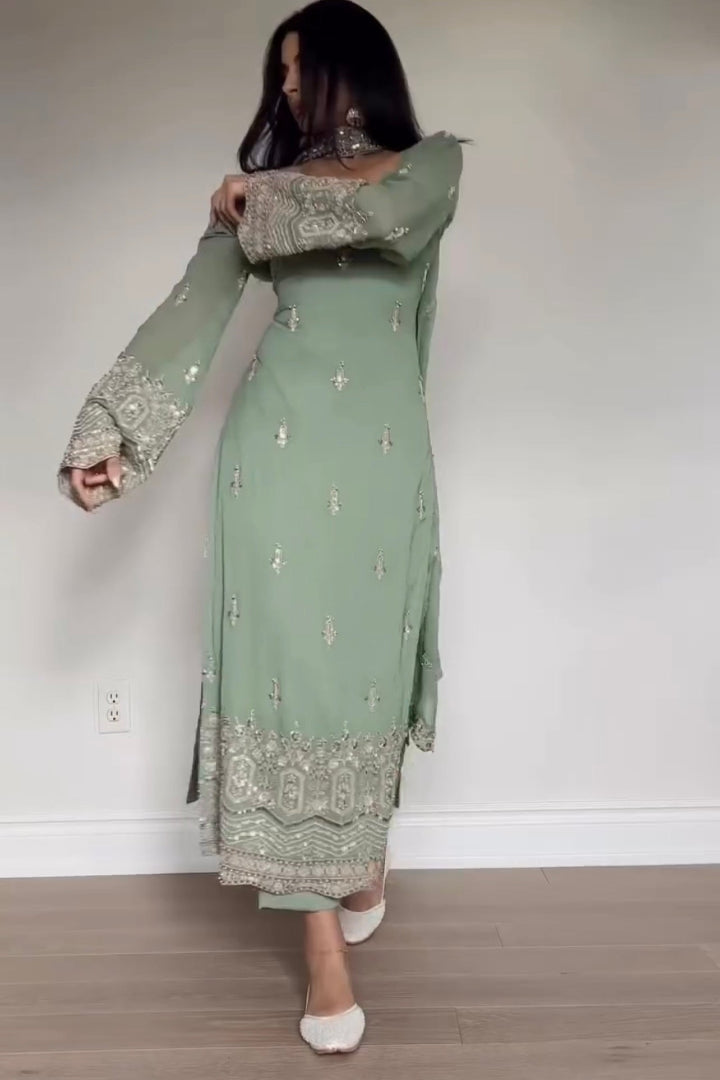 Person wearing a green embroidered outfit against a plain background
