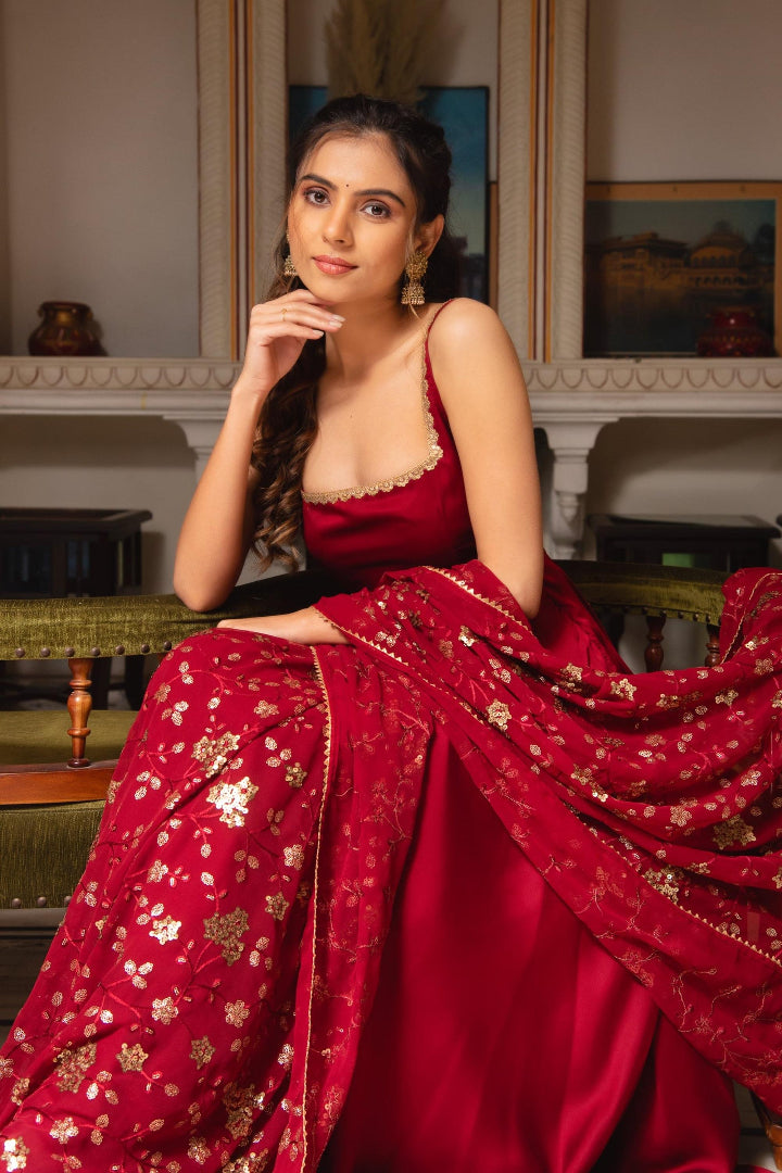 Woman in a red saree with gold patterns sitting indoors.