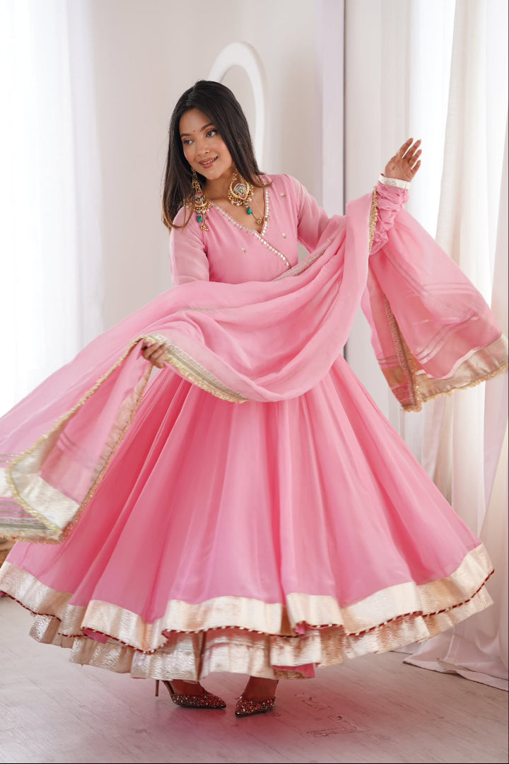 Woman wearing a pink traditional outfit with gold accents in a bright room.