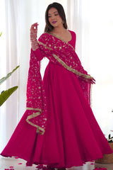 Woman wearing a pink saree with gold details against a white curtain background