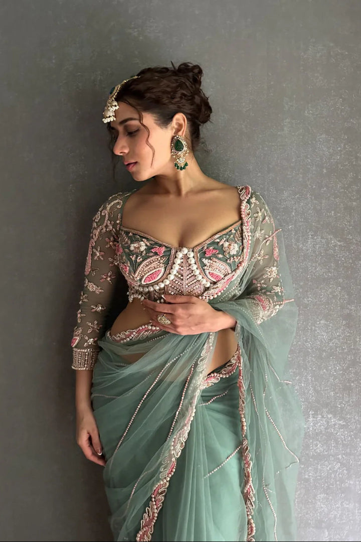 Woman wearing a traditional embroidered blouse and light green saree against a gray background