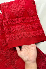 Red embroidered fabric held by a hand against a white background