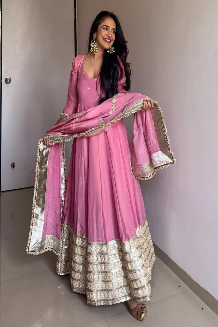 Woman in a pink traditional outfit with gold details indoors.