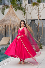 Woman in a bright pink traditional outfit standing by a poolside with plants in the background