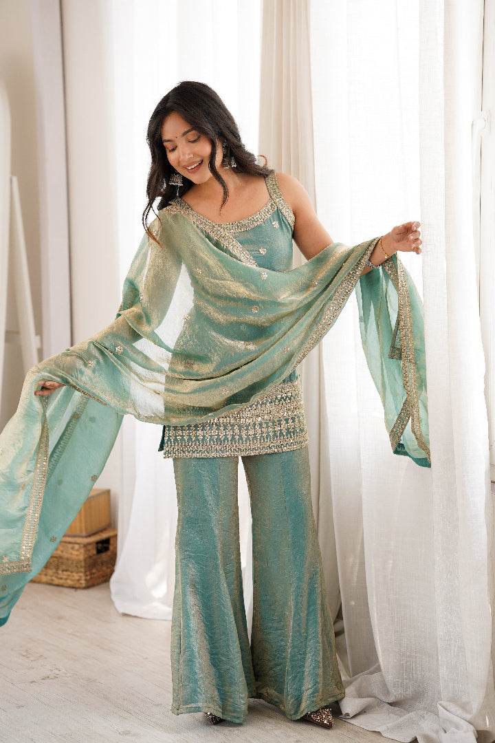 Woman wearing a teal and gold traditional outfit with a matching dupatta in a bright room.
