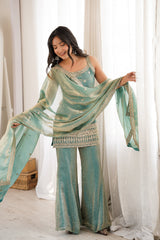 Woman wearing a teal and gold traditional outfit with a matching dupatta in a bright room.