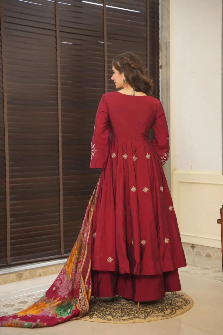 Woman in a red traditional outfit with a colorful dupatta, standing in a room with wooden shutters.