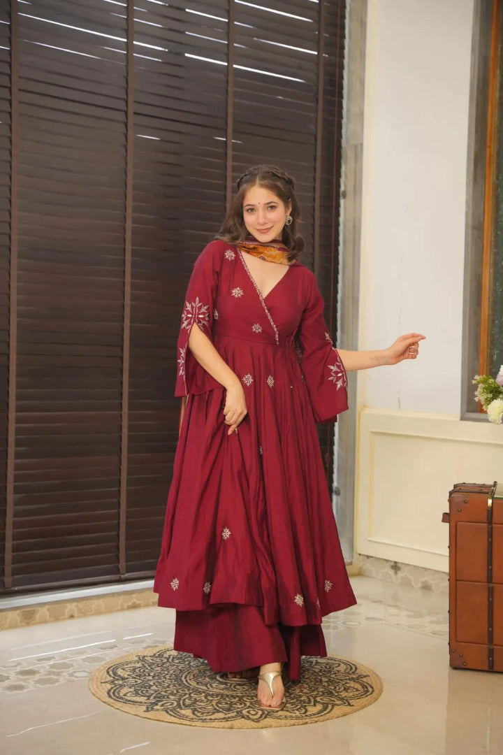 Woman in a red traditional outfit standing in a room with a window and decorative rug.