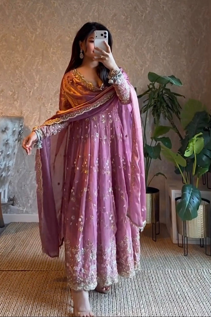 Woman taking a mirror selfie wearing a pink and orange traditional outfit in a room with plants and furniture.