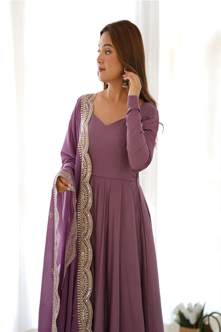 Woman wearing a long purple dress with a matching shawl in a bright room.
