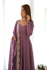Woman wearing a long purple dress with a matching shawl in a bright room.