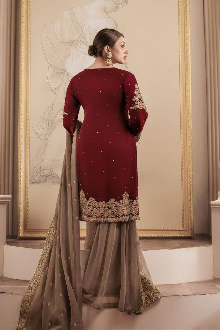Woman in a maroon and gold traditional outfit standing in an elegant interior setting.
