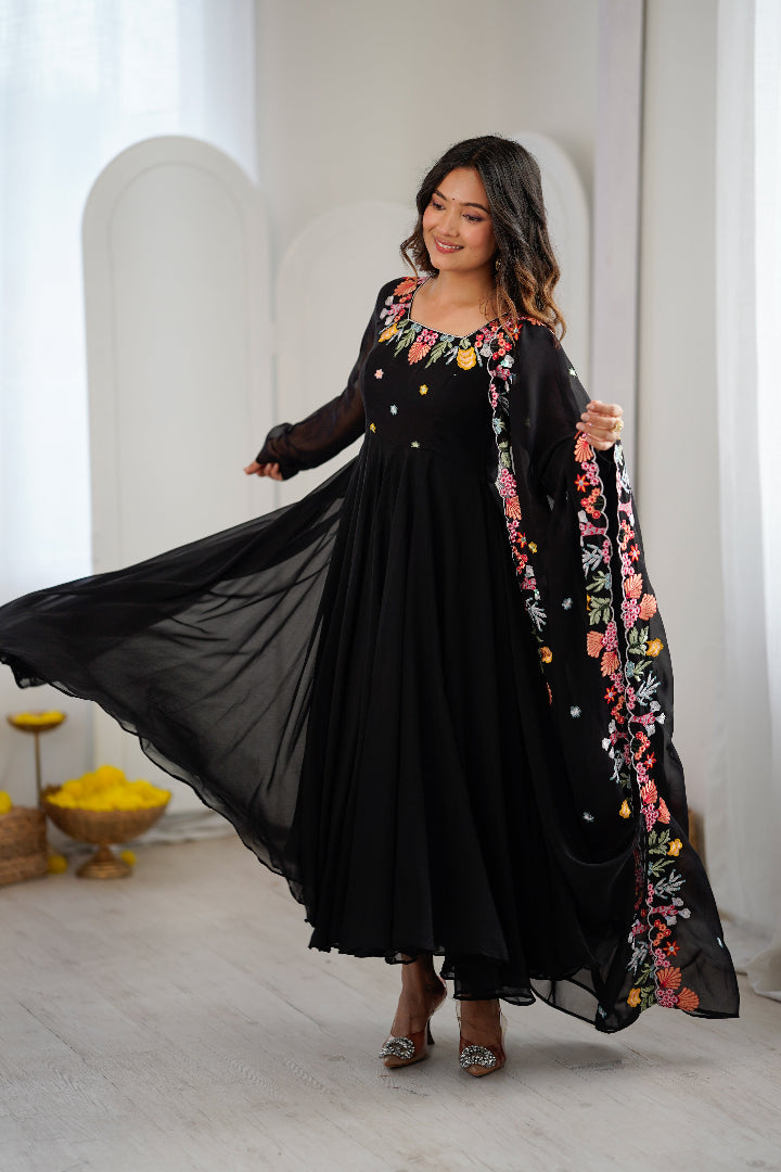 A woman modeling a black maxi dress with colorful floral embroidery 