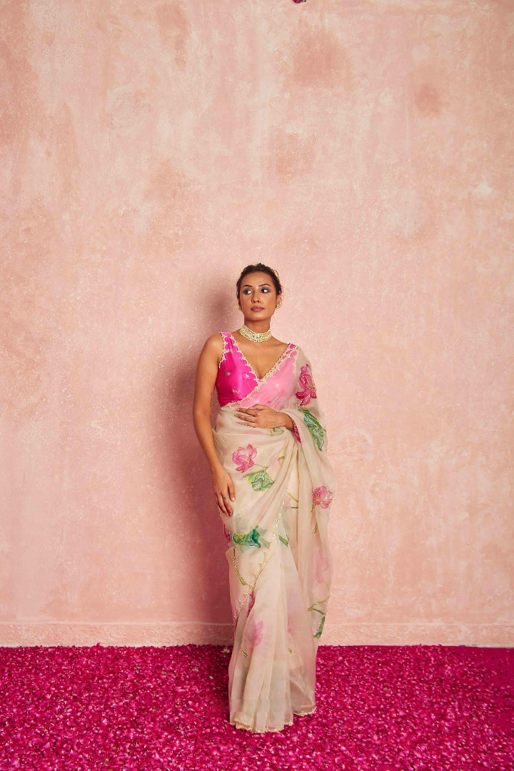 Woman wearing a floral saree with a pink blouse against a pink background