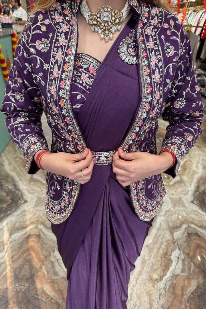 Woman wearing a purple dress with a floral jacket against a stone wall background