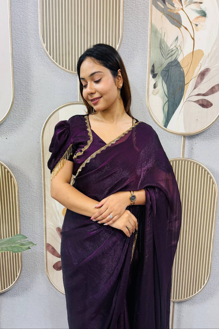 Woman in a purple saree standing against a decorative wall with floral patterns.
