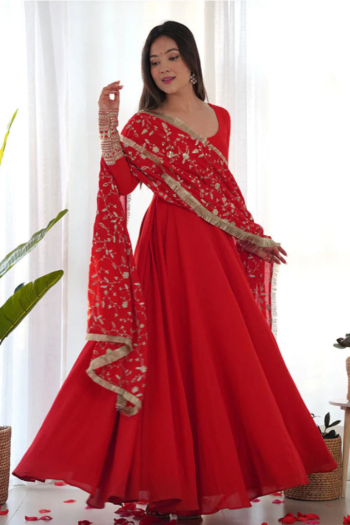 Woman in a red traditional outfit with gold details in a bright room.